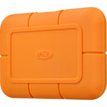 Load image into Gallery viewer, The orange LaCie Rugged 1TB USB-C Mobile SSD with its protective bumper, shown next to a laptop on a desk.