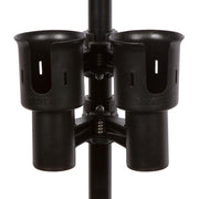 The black RoboCup dual drink holder clamped securely to the arm of a white patio chair, holding two beverage cans.